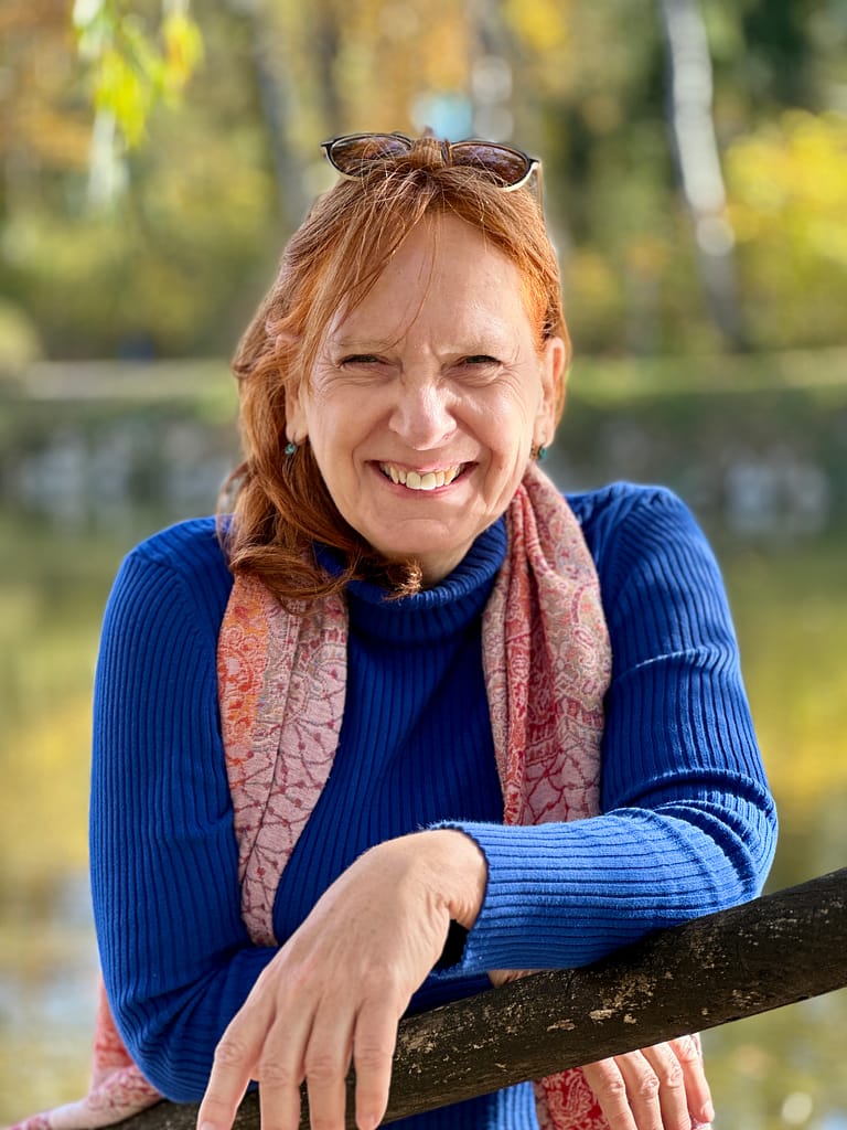 Eine Frau in einem blauen Pullover lehnt an einem Geländer in einem Park und fängt die friedliche Atmosphäre von NL-Danke ein.